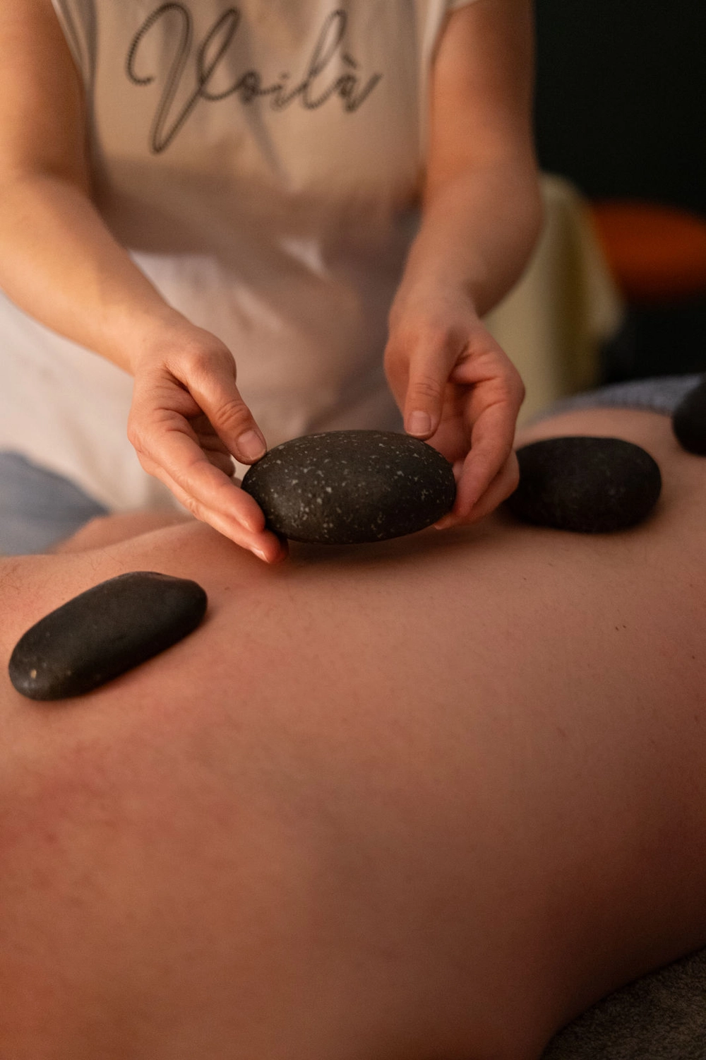 Energie Stüberl - Marianne Roßmadl - Energetische Heilarbeit und Massage - Person legt während einer Hot-Stone-Massagetherapie glatte schwarze heiße Steine auf einen nackten Rücken